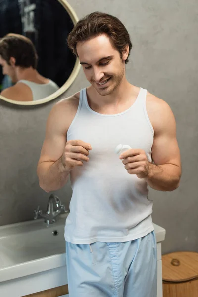 Happy man in white tank top holding dental floss in bathroom — Stock Photo
