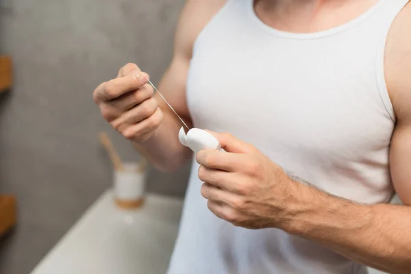 Partial view of man in white tank top holding dental floss in bathroom — Stock Photo