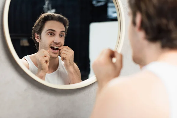 Giovane uomo filo interdentale denti vicino specchio in bagno — Foto stock