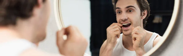 Jeune homme regardant dans le miroir tout en passant la soie dentaire le matin, bannière — Photo de stock