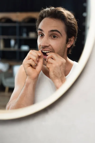 Jovem limpando dentes com fio dental perto do espelho — Fotografia de Stock