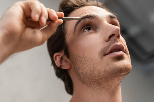 Close up view of young man tweezing eyebrows in morning — Stock Photo