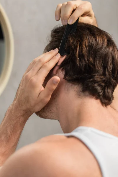 Jeune homme brunette peigner les cheveux dans la salle de bain — Photo de stock