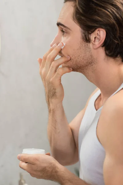 Vue latérale du jeune homme appliquant de la crème visage le matin — Photo de stock