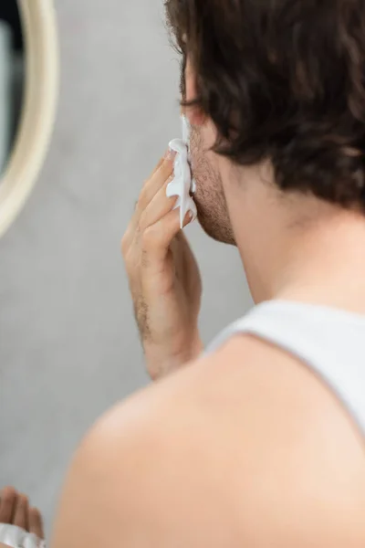 Visão parcial do homem desfocado aplicando espuma de barbear no rosto — Fotografia de Stock