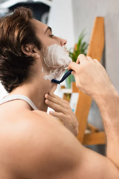 Brunette homme rasage avec rasoir de sécurité dans la salle de bain — Photo de stock