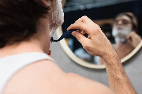 Blurred man shaving with safety razor near mirror in bathroom — Stock Photo