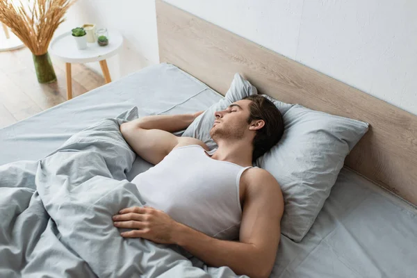 Junger brünetter Mann schläft im Bett unter blauer Decke — Stockfoto