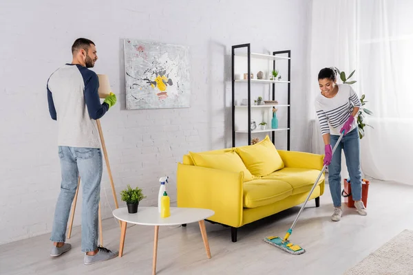 Smiling african american woman cleaning floor near boyfriend at home — Stock Photo