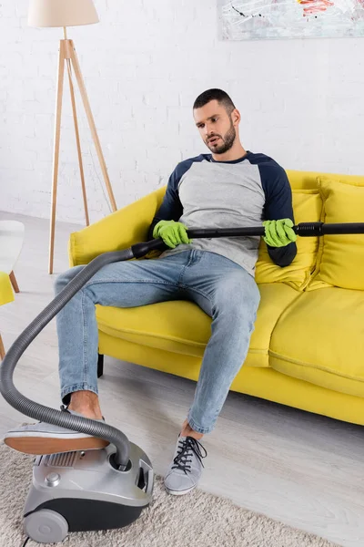 Jeune homme tenant aspirateur sur le canapé — Photo de stock