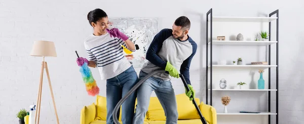 Smiling african american woman with dust brush having fun with boyfriend at home, banner — Stock Photo