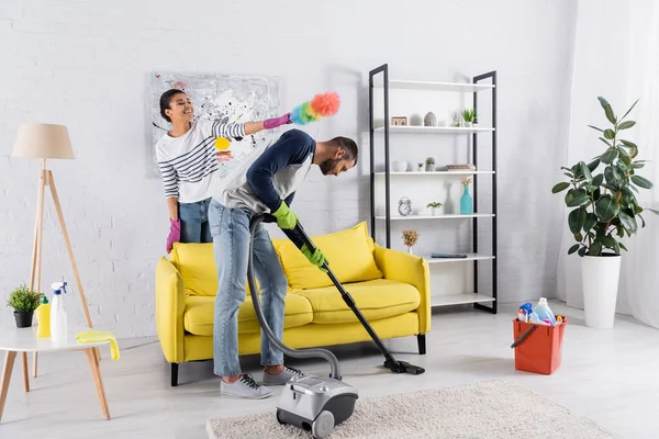 Smiling african american woman holding dust brush near boyfriend cleaning floor — Stock Photo