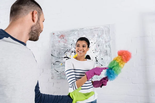 Cheerful african american woman pointing at dust brush near boyfriend — Stock Photo