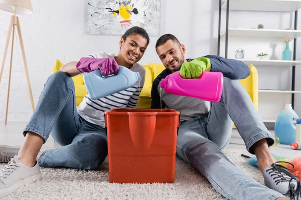 Smiling african american woman pouring detergent in bucket near boyfriend — Stock Photo
