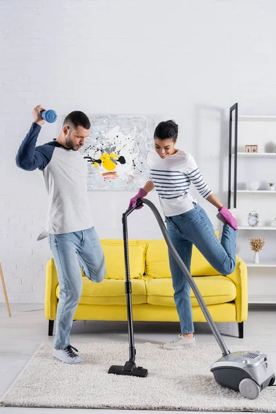 Joven pareja interracial bailando mientras limpia la sala de estar - foto de stock