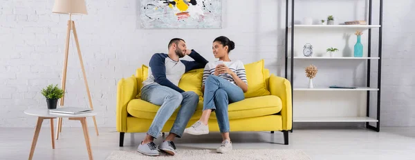 Sonriente pareja multiétnica hablando en la sala de estar, pancarta - foto de stock