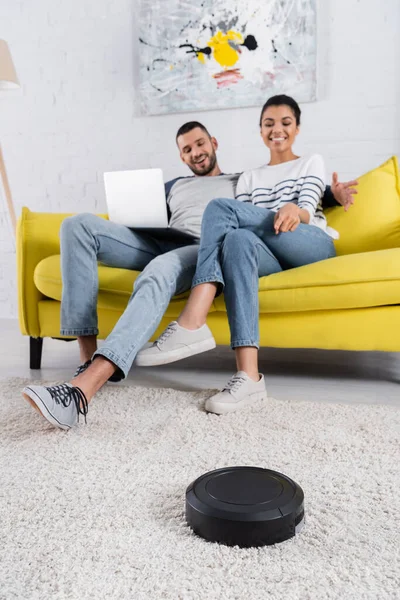 Robotique aspirateur près flou couple interracial avec ordinateur portable — Photo de stock