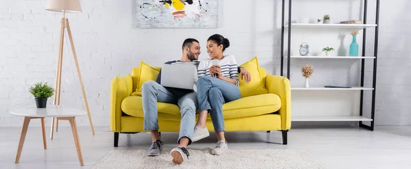 Jovem casal multiétnico usando gadgets no sofá, banner — Fotografia de Stock