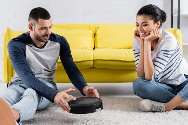 Man holding robotic vacuum cleaner near african american girlfriend — Stock Photo