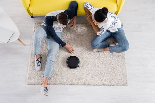 Overhead view of multiethnic couple sitting near robotic vacuum cleaner — Stock Photo