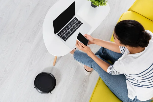 Overhead view of african american freelancer using smartphone near robotic vacuum cleaner — Stock Photo