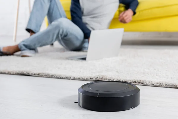 Cropped view of robotic vacuum cleaner on floor near man using laptop at home — Stock Photo