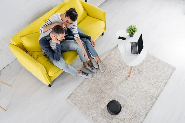 Overhead view of smiling african american woman pointing at robotic vacuum cleaner near boyfriend — Stock Photo