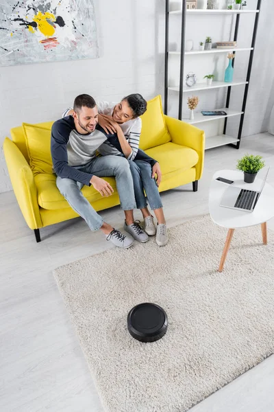 Smiling african american woman embracing boyfriend near robotic vacuum cleaner and devices — Stock Photo