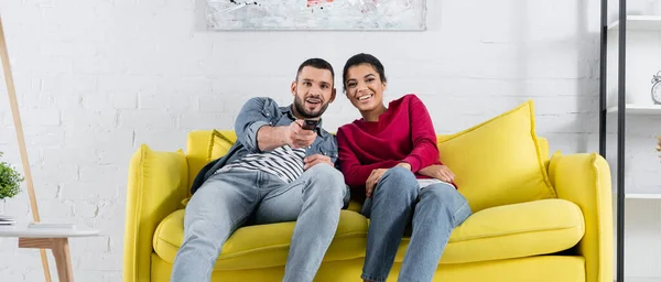 Sorridente coppia interrazziale guardando la tv sul divano, banner — Foto stock