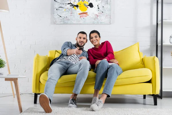 Jeune couple multiethnique regardant un film sur le canapé à la maison — Photo de stock
