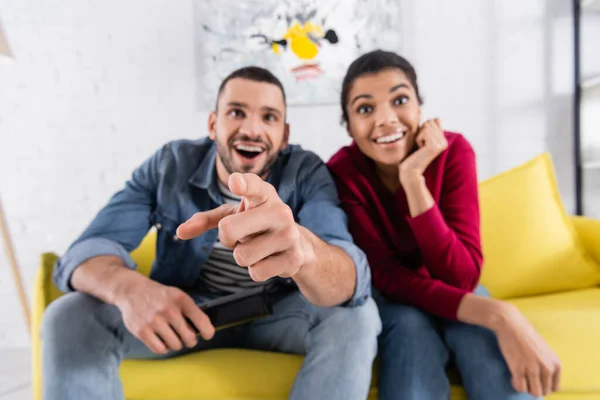 Borroso hombre excitado apuntando a la cámara cerca de la novia afroamericana — Stock Photo