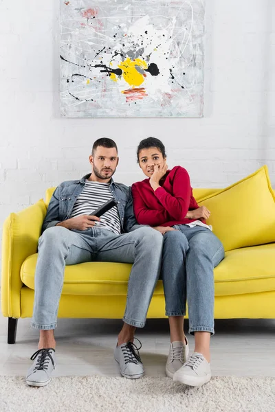 Scared african american woman sitting near boyfriend with remote controller — Stock Photo