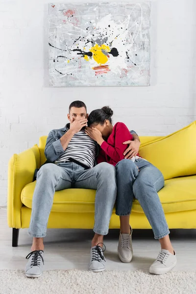 Femme afro-américaine se cachant près du petit ami effrayé et télécommande — Photo de stock