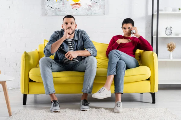 Hombre enfocado sosteniendo mando a distancia cerca de novia hablando en el teléfono celular - foto de stock