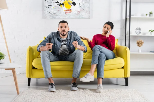 Afro americana mujer hablando en smartphone cerca concentrado novio viendo tv - foto de stock