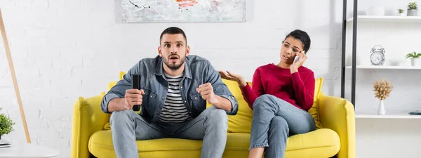 African american woman talking on mobile phone near boyfriend watching tv, banner — Stock Photo