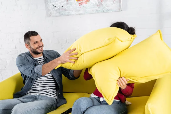 Positivo uomo cuscino lotta con la fidanzata afro-americana in soggiorno — Foto stock