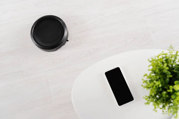 Top view of robotic vacuum cleaner on floor near smartphone on coffee table — Stock Photo