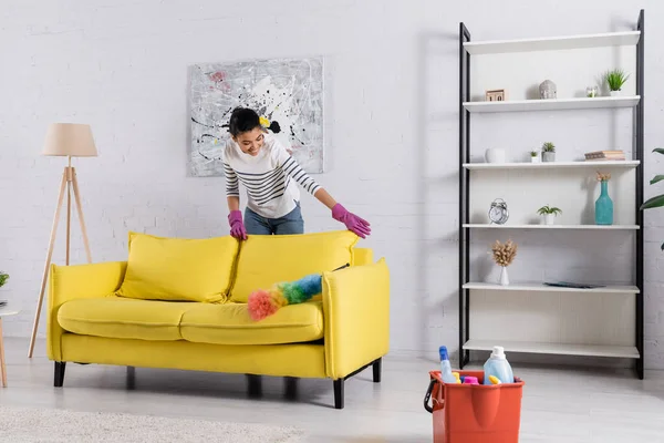 Junge Afroamerikanerin putzt Couch in der Nähe von Staubbürste und Waschmitteln — Stockfoto