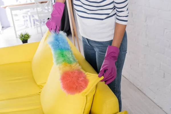 Vue recadrée de la femme en gants de caoutchouc nettoyage canapé avec brosse à poussière — Photo de stock