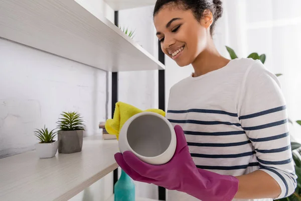 Sonriente mujer afroamericana limpiando jarrón en casa - foto de stock