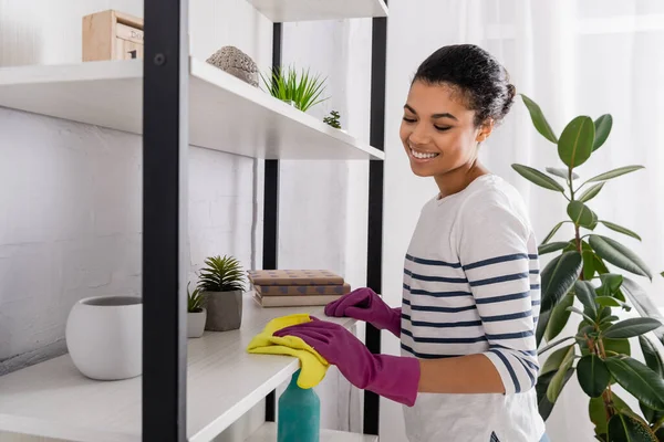 Mujer afroamericana sonriente en guantes de goma limpiando armario - foto de stock