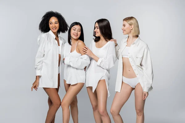 Grupo de alegres modelos multiétnicos sonriendo aislados en gris - foto de stock