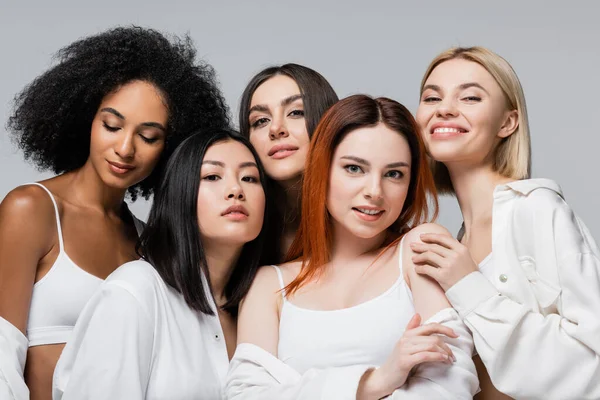 Asiático e africano americano modelos no branco camisas posando com alegre mulheres isolado no cinza — Stock Photo