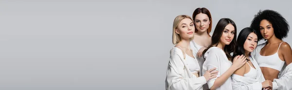 Modelos americanos asiáticos y africanos en camisas blancas posando con mujeres jóvenes aisladas en gris, bandera - foto de stock