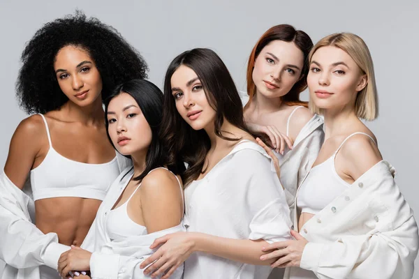 Brunette asian and african american models in white shirts posing with young women isolated on grey — Stock Photo