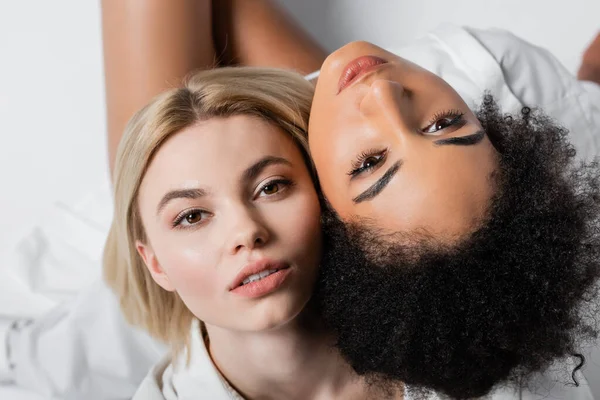 Vue du dessus du modèle afro-américain près de femme blonde regardant la caméra sur blanc — Photo de stock