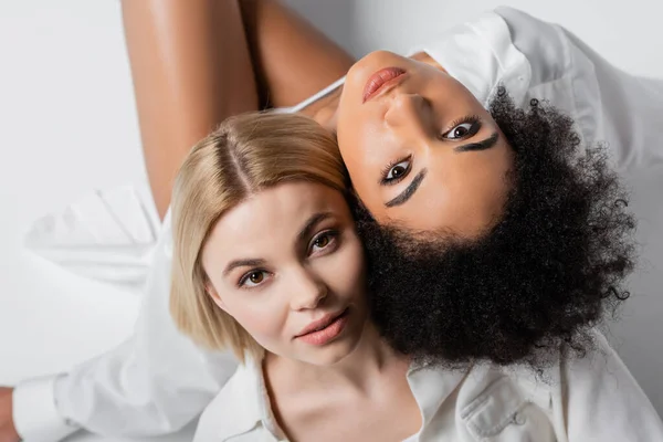 Draufsicht auf multiethnische brünette und blonde Models, die in die Kamera auf weiß schauen — Stockfoto