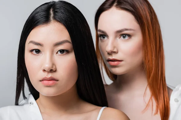 Asian model posing with blurred redhead woman isolated on grey — Stock Photo