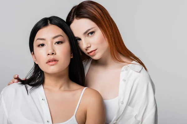 Brunette asian woman and redhead model posing isolated on grey — Stock Photo